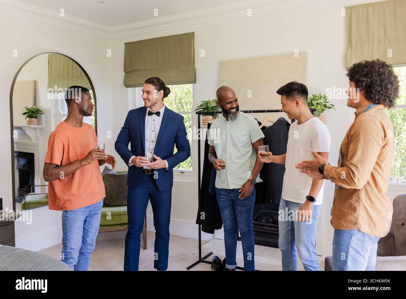 Sposo in tuta ridendo con gli amici a casa, godendosi la festa pre-matrimonio Foto Stock