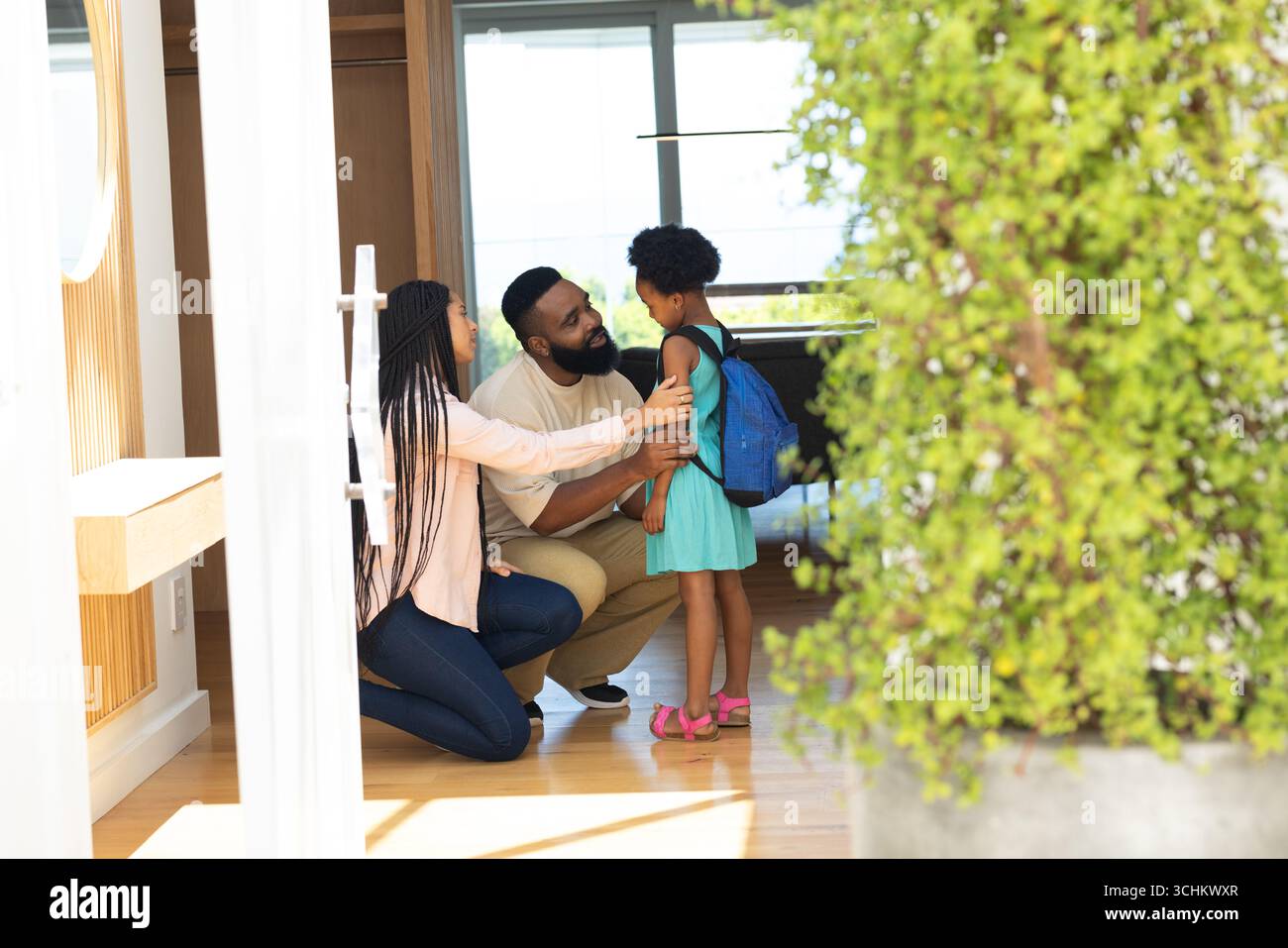 I genitori aiutano la figlia con lo zaino, si preparano per la scuola a casa Foto Stock