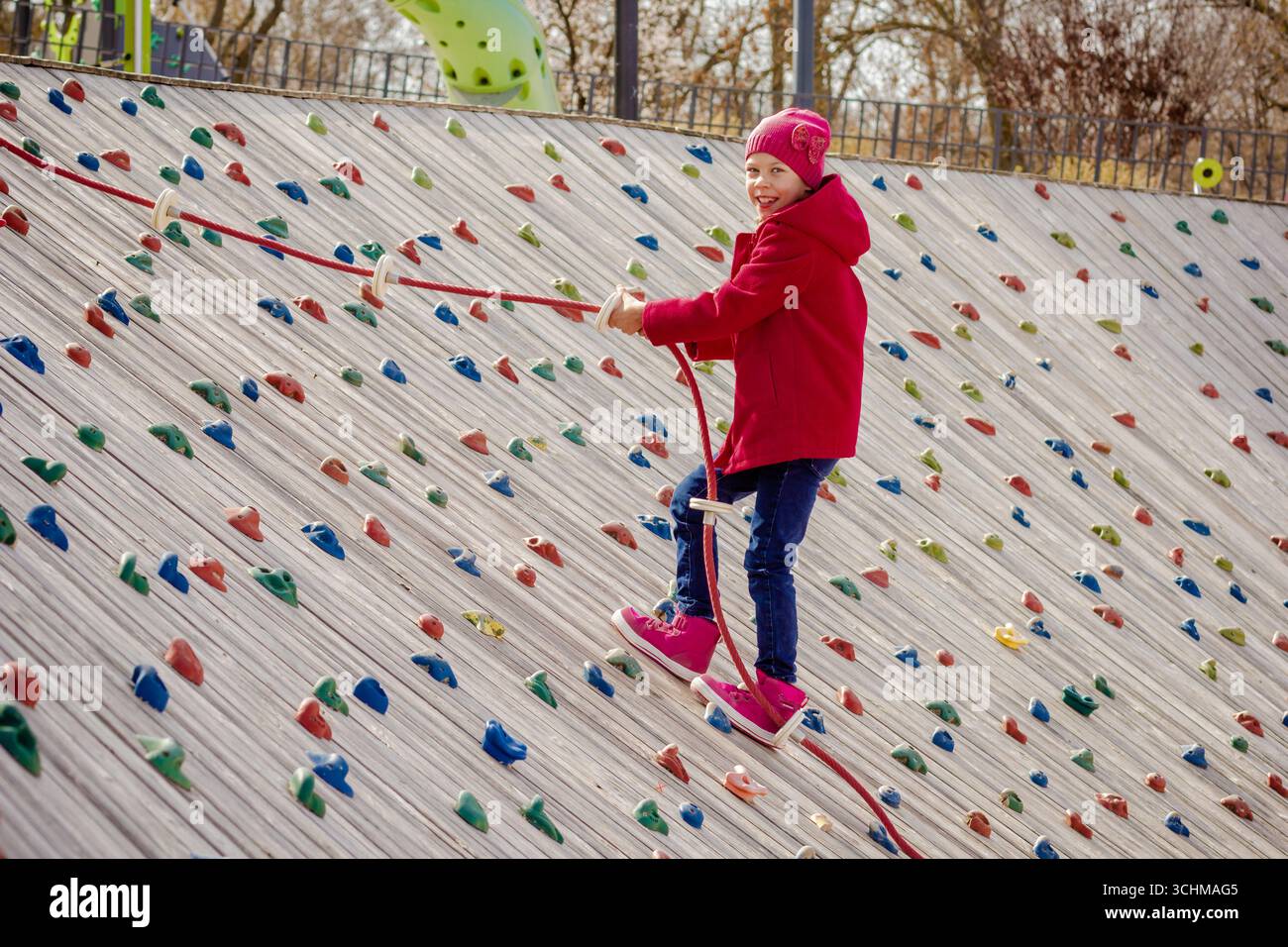 Bambino felice che si arrampica su una parete di roccia artificiale usando la corda sul parco giochi Foto Stock