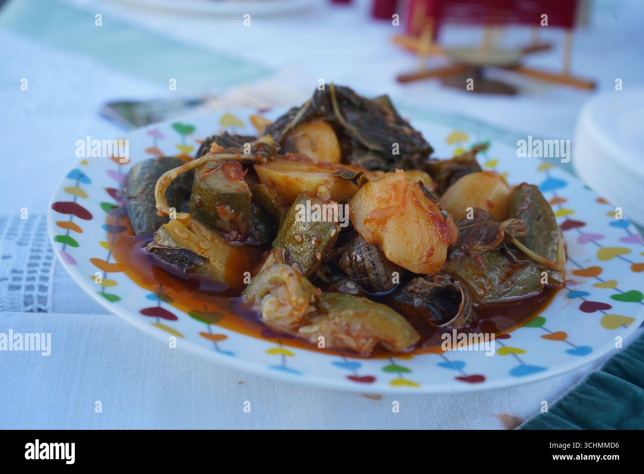 Primo piano di un piatto cretese con lumache, zucchine, patate e verdure in salsa di pomodoro. Gastronomia cretese, cucina greca, dieta mediterranea. Foto Stock
