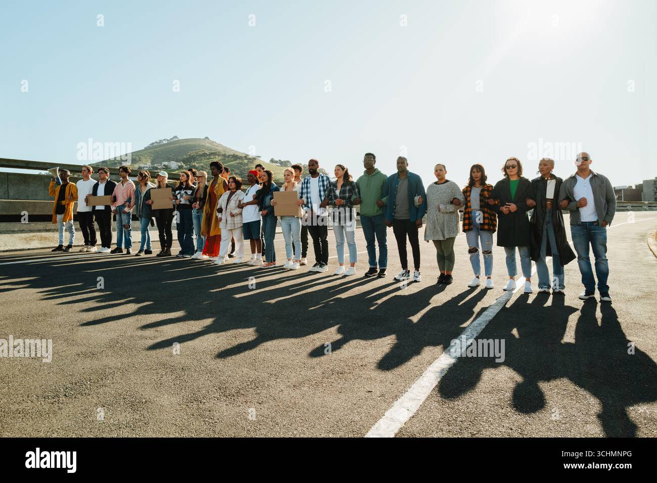 Un gruppo numeroso e diversificato di persone all'aperto che si tengono per mano in unità. Il gruppo comprende uomini e donne di varie età e schieramenti etnici Foto Stock