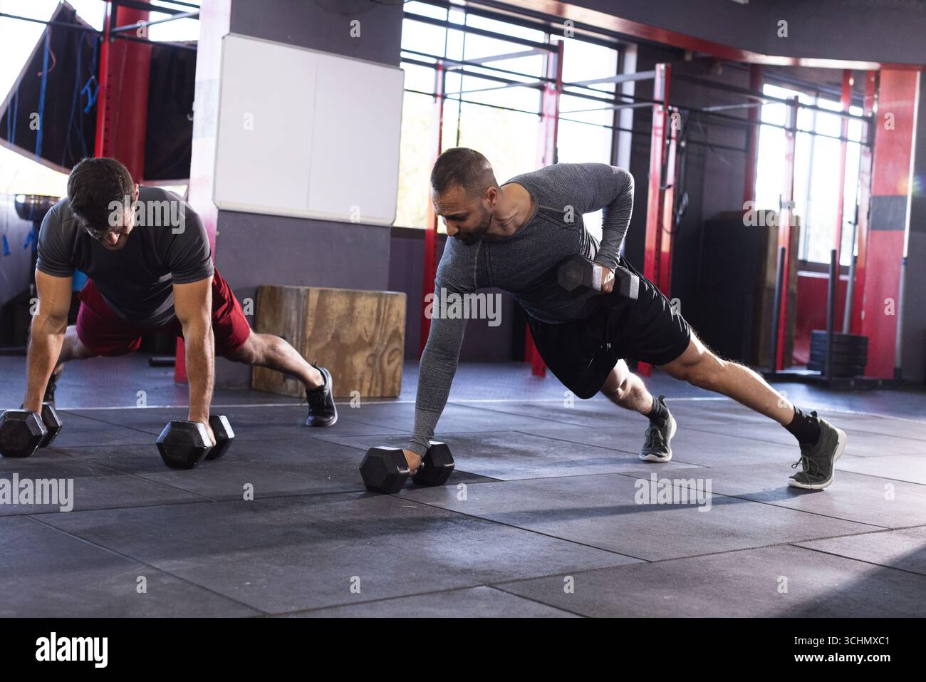 Diversi partner maschili che eseguono file di tavole su tappetino in palestra utilizzando manichini esagonali Foto Stock