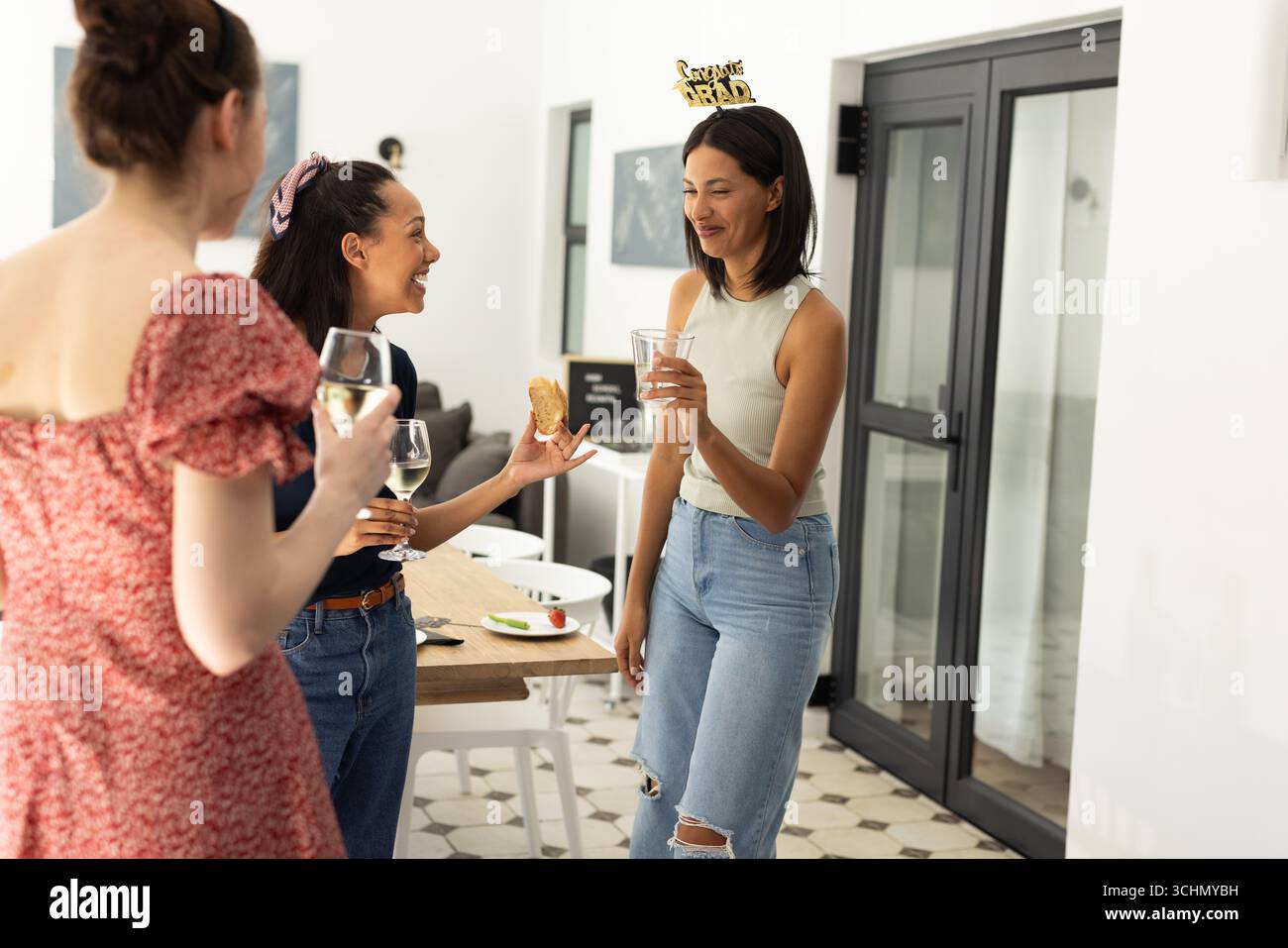 Ridendo e chiacchierando, tre giovani donne si godono un drink a casa Foto Stock