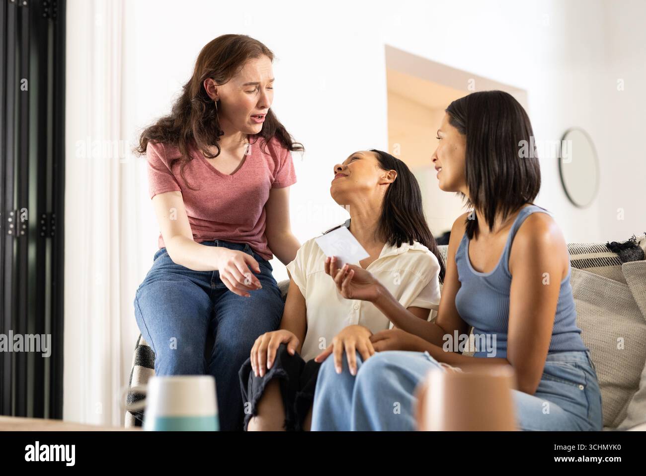 Ridendo insieme su un comodo divano, tre giovani donne condividono un momento di gioia Foto Stock Ridendo insieme su un comodo divano, tre giovani donne condividono un momento di gioia Foto Stock