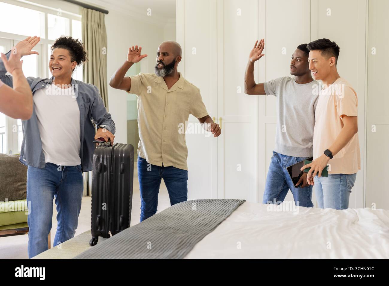 Amici che festeggiano in camera da letto, con valigia e smartphone Foto Stock