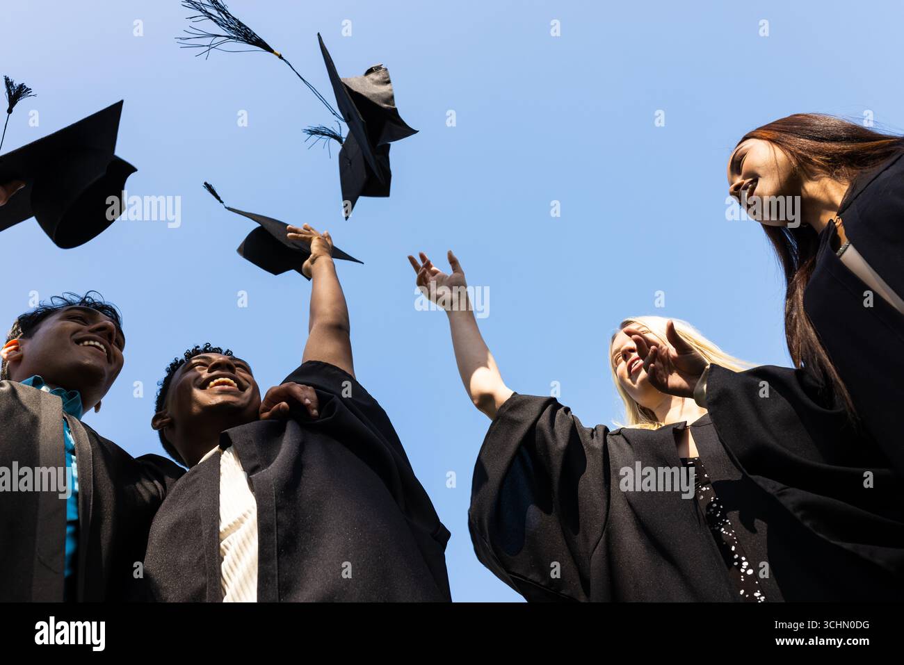 Diversi laureati festeggiano lanciando berretti in aria, allegri ed eccitati, spazio copia Foto Stock