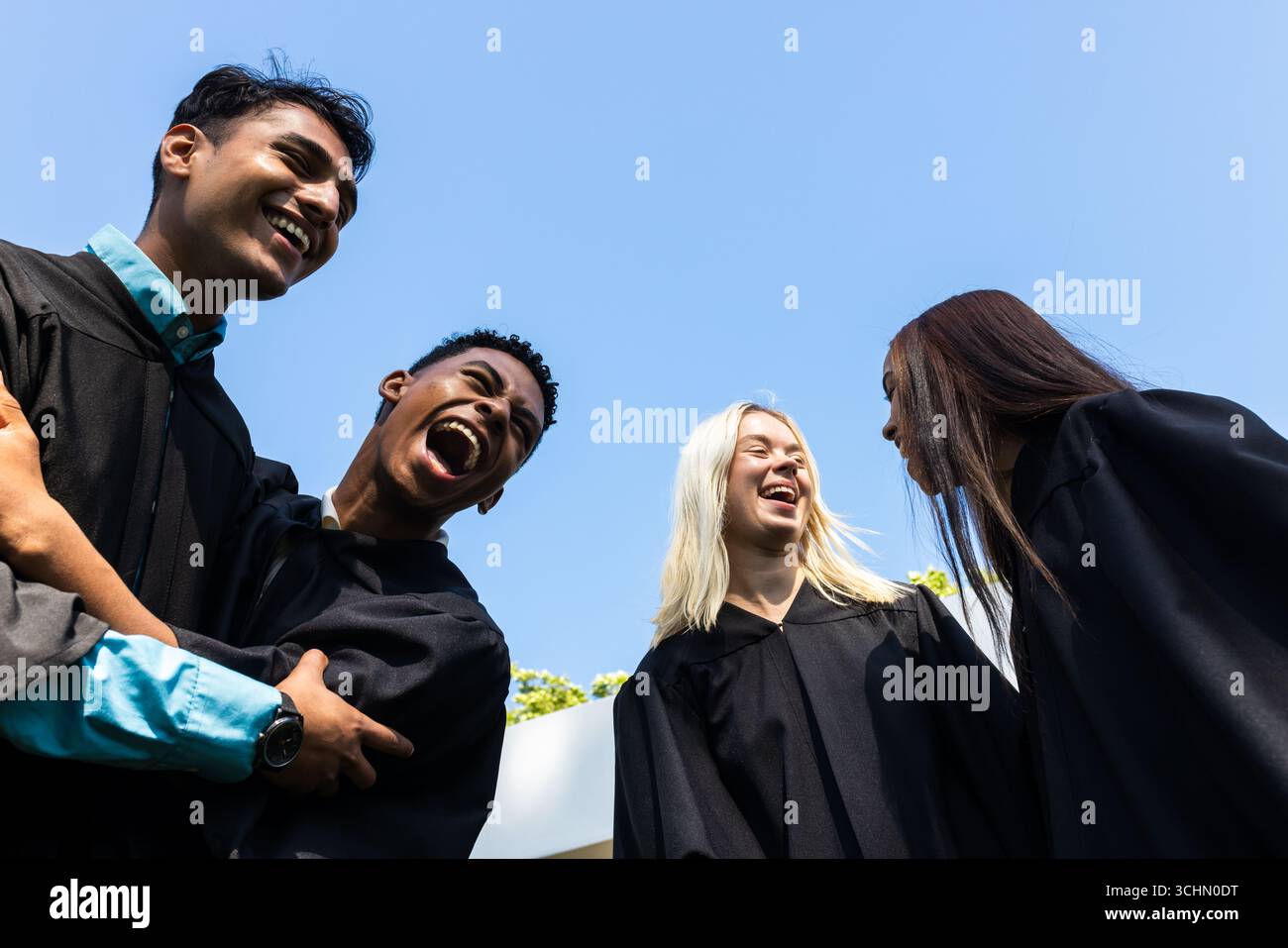 Diversi laureati in abiti che celebrano i risultati raggiunti, ridendo gioiosamente in giardino, spazio copia Foto Stock
