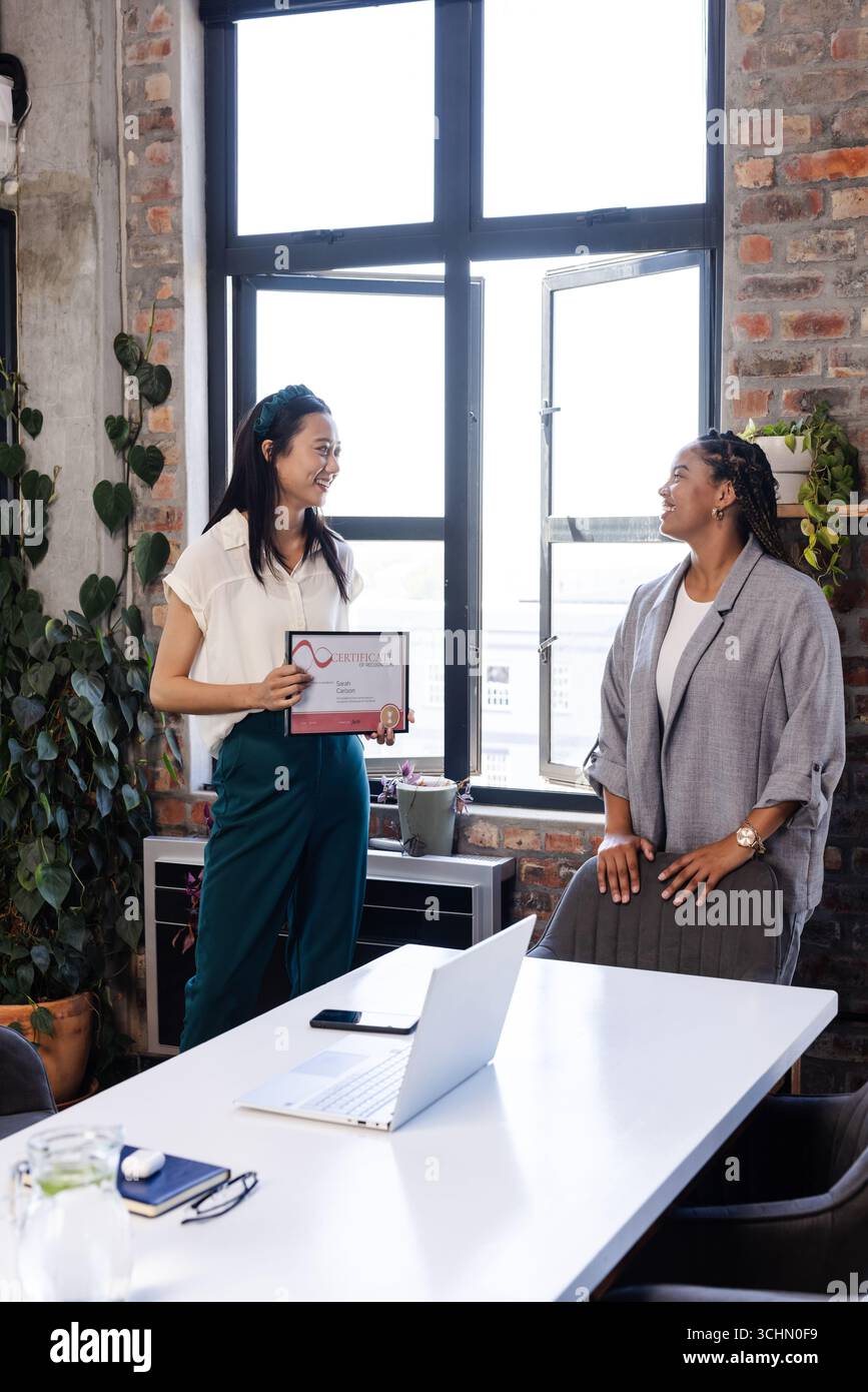 Donna asiatica in possesso di certificato sorridente con collega in ufficio moderno Foto Stock
