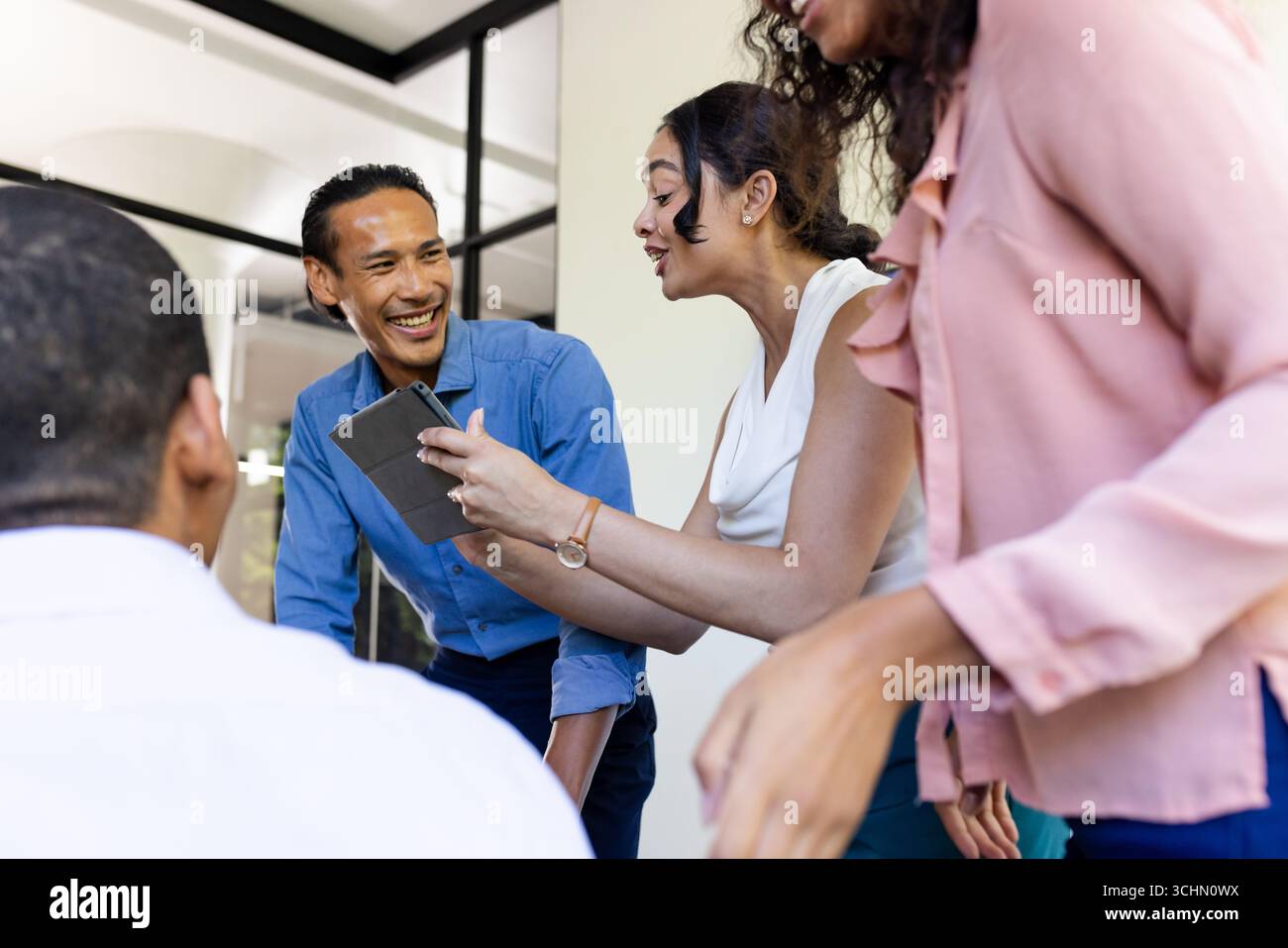 Team aziendale diversificato che collaborano con tablet, condividono idee e sorridono in ufficio Foto Stock