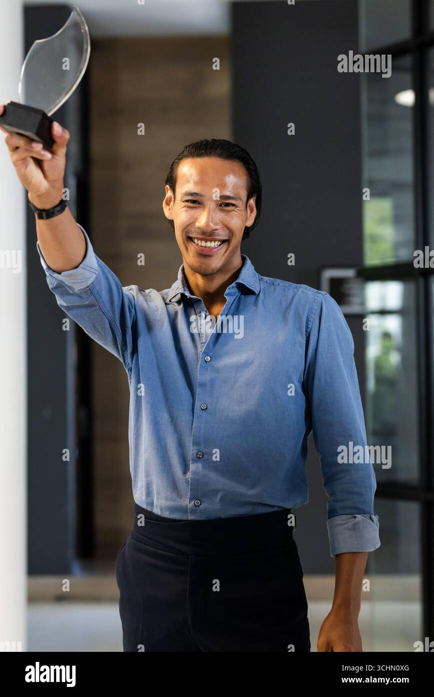 Uomo sorridente che tiene un premio in carica, celebra il successo e il successo Foto Stock