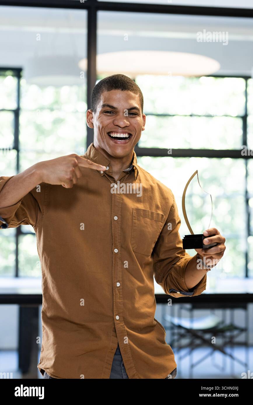 Uomo sorridente che tiene un premio in carica, celebra i risultati con entusiasmo Foto Stock