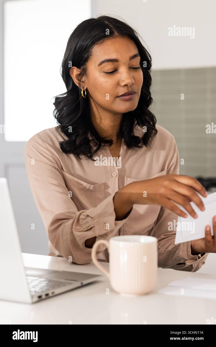 donna che legge una lettera a casa con un computer portatile e una tazza da caffè Foto Stock donna che legge una lettera a casa con un computer portatile e una tazza da caffè Foto Stock