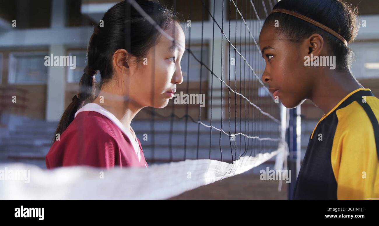 Affrontare giocatori di pallavolo adolescenti che indossano maglie rosse e gialle-nere nella palestra scolastica, vicino alla rete Foto Stock