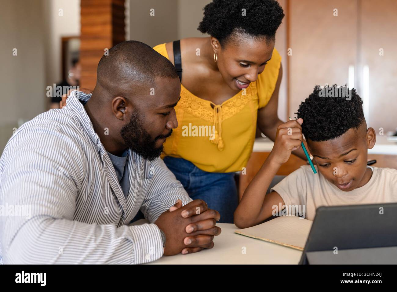 Genitori che aiutano il figlio con i compiti a casa utilizzando un tablet, concentrandosi sull'apprendimento Foto Stock