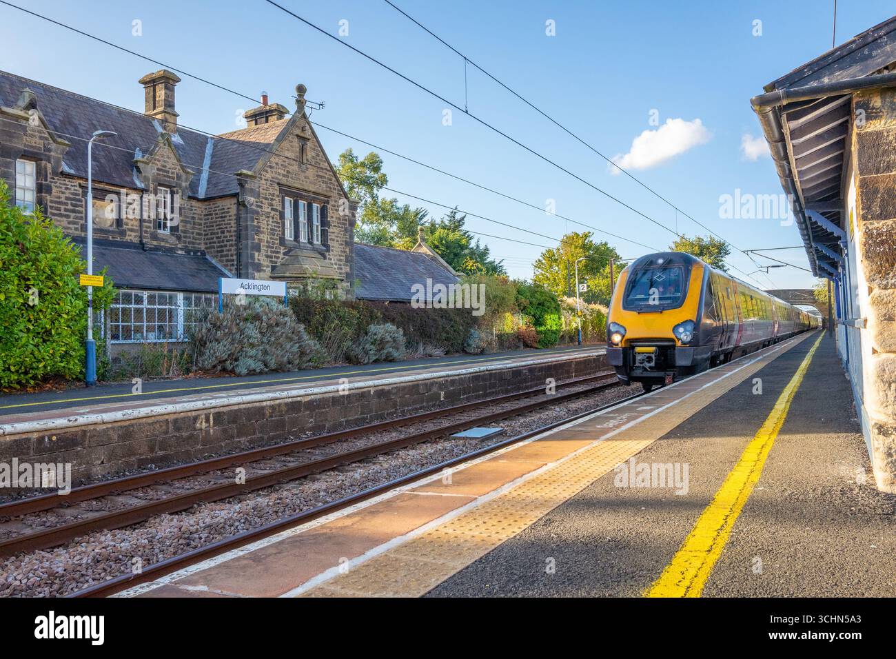 Treni da fondo Voyager o Super Voyager (Classe 220 e Classe 221) che passano attraverso la stazione ferroviaria di Acklington costruita in pietra vittoriana. Foto Stock