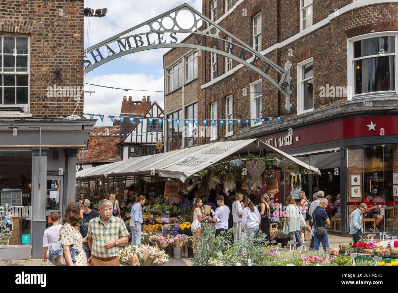 Shambles Market a York, in Inghilterra, con bancarelle di fiori e folle di acquirenti sotto il tetto, creando una vivace scena di commercio e comunità locale. Foto Stock