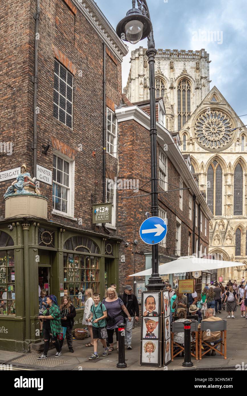 York Minster vista da Minster Gates di York, Inghilterra, con architettura gotica, edifici storici e turisti felici di passaggio. Foto Stock