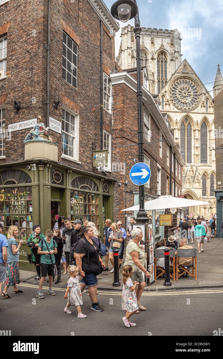 Turisti e gente del posto vicino alla York Minster e alla Minster Gates di York, Inghilterra, con architettura storica e la statua di Minerva sopra il negozio all'angolo Foto Stock