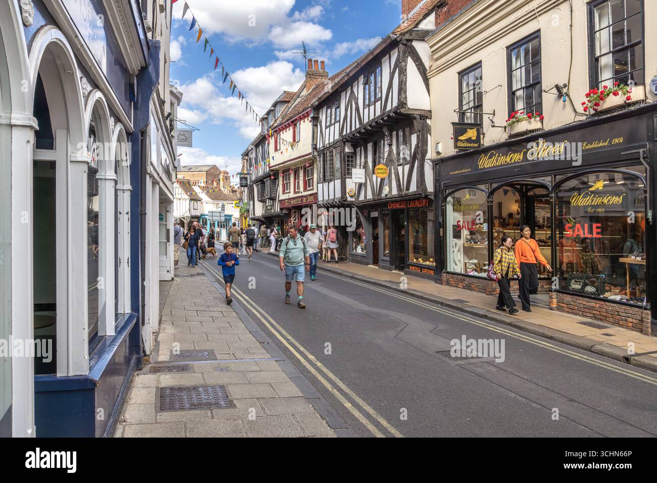 I pedoni passeranno davanti a edifici e negozi in legno incorniciati in una vivace strada di York, Inghilterra, decorata con grappolo e attiva con il turismo. Foto Stock