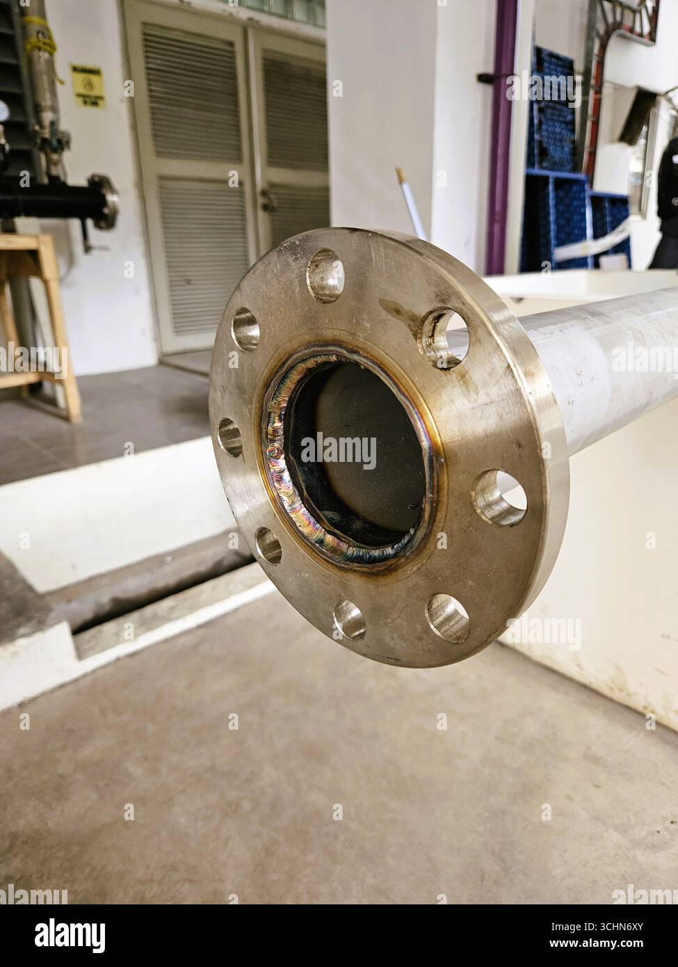 Primo piano della flangia del tubo metallico in un impianto industriale, parte di un sistema meccanico per il collegamento dei fluidi - Immagine stock catturata con smartphone