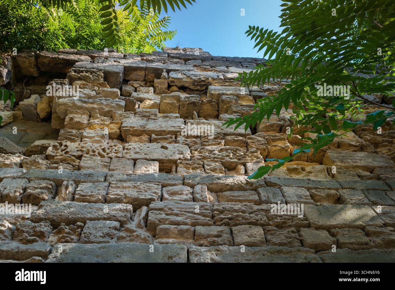 Il vecchio muro di pietra calcarea gialla si deteriora lentamente e si rompe a causa dell'esposizione ambientale Foto Stock