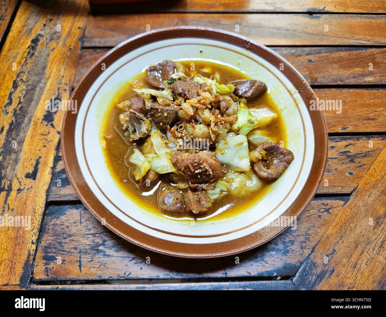 Tradizionale stufato di carne indonesiano servito su piatto con verdure e ricca salsa al curry giallo - Immagine stock catturata con smartphone