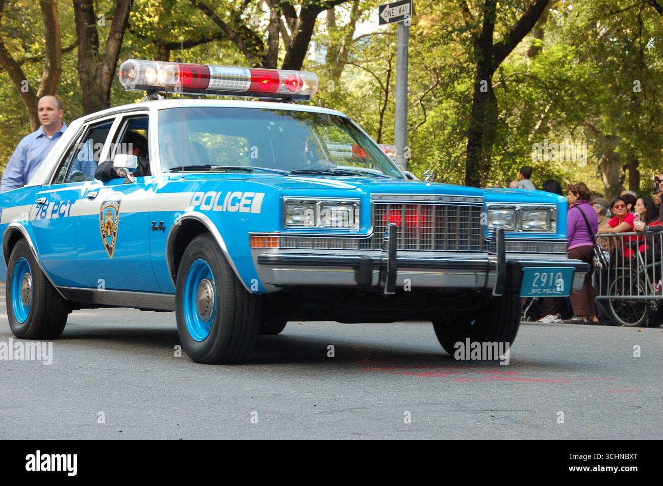 Auto della polizia di New York blu d'epoca con luci lampeggianti che guidano alla Columbus Day Parade di New York, circondata da persone e alberi Foto Stock