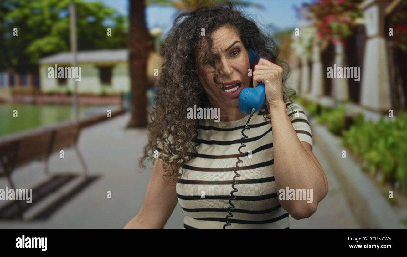 Donna che tiene il ricevitore del telefono all'orecchio con la mano sulla fronte in strada; frustrazione di comunicazione. Foto Stock