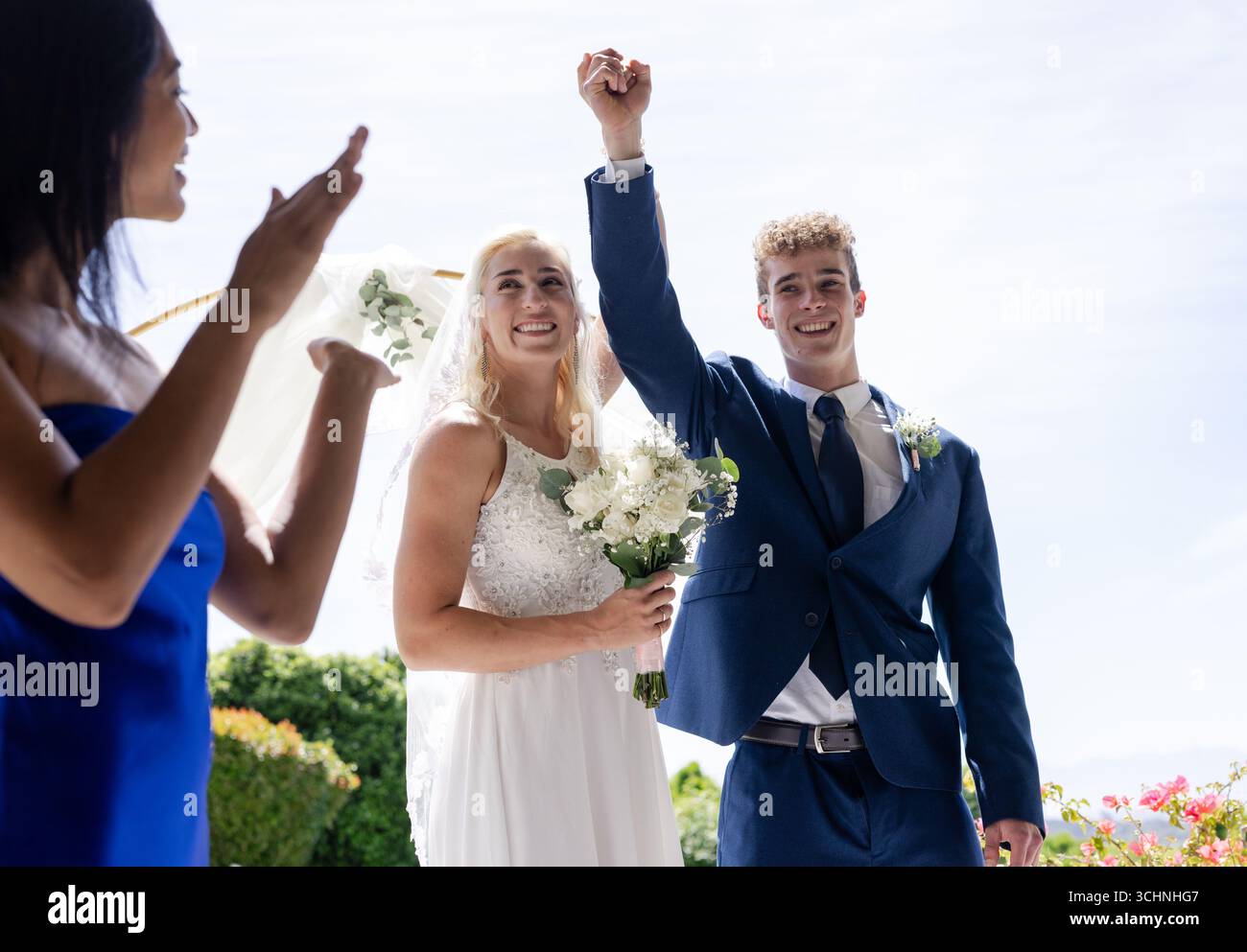 Sposa e sposo festeggiano all'aperto, tenendosi per mano e sorridendo gioiosamente Foto Stock