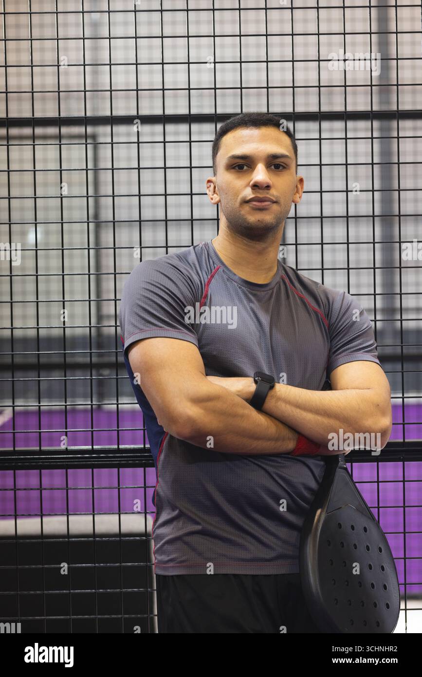 Atleta maschile in camicia e pantaloncini sportivi in posa con racchetta in padel e smartwatch sul campo del padel Foto Stock