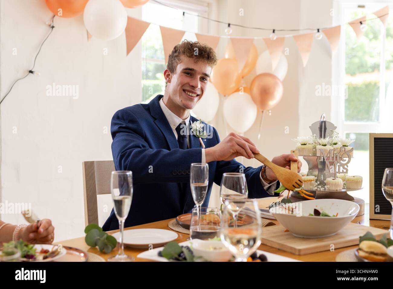 Sposo sorridente in tuta che serve cibo al ricevimento di nozze con arredi festivi Foto Stock