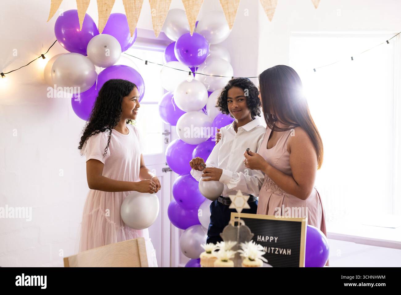Famiglia diversificata, che celebra bat mitzvah, palloncini e decorazioni che condividono momenti di gioia, a casa Foto Stock