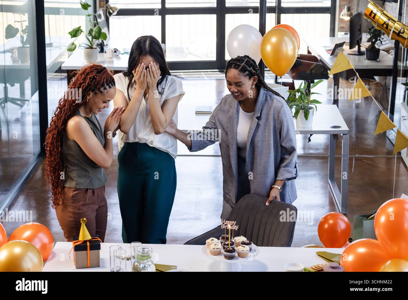 Colleghi di sesso femminile che celebrano una festa a sorpresa in ufficio con palloncini e cupcake Foto Stock