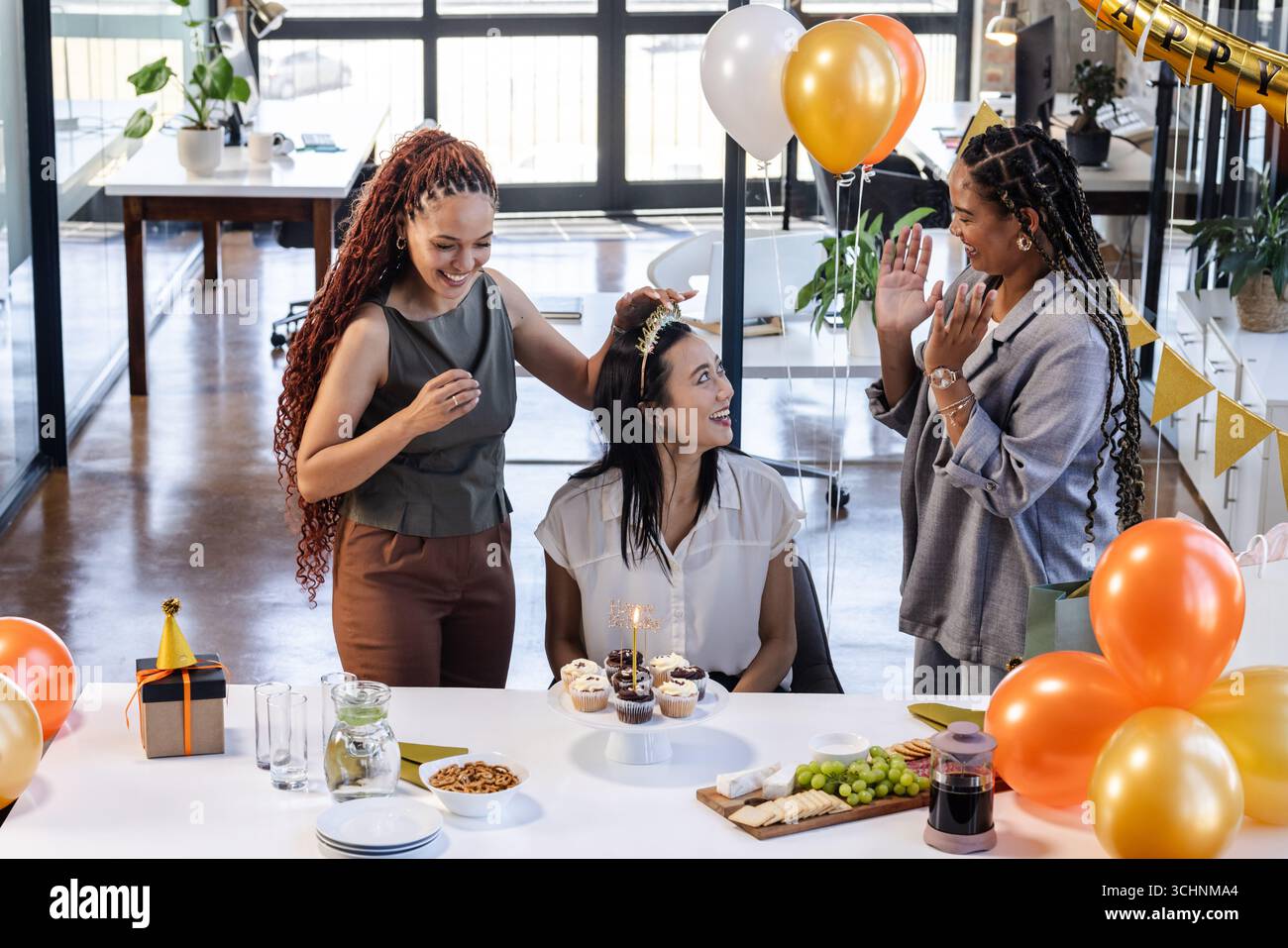 Colleghi di sesso femminile che festeggiano il compleanno con cupcake e palloncini in un ufficio moderno Foto Stock