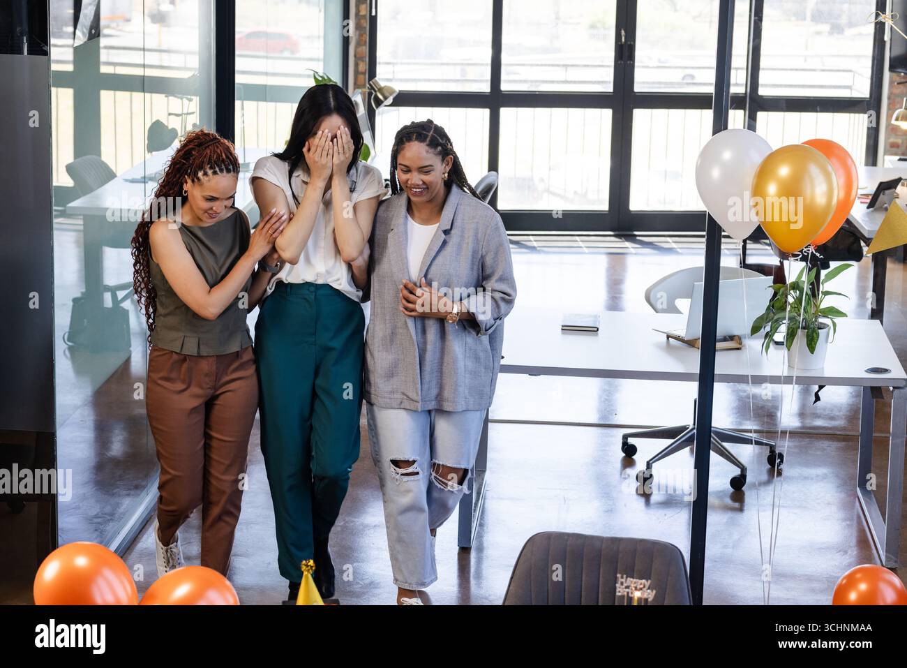 Colleghi di sesso femminile che celebrano una festa a sorpresa in un ufficio moderno con palloncini e risate Foto Stock