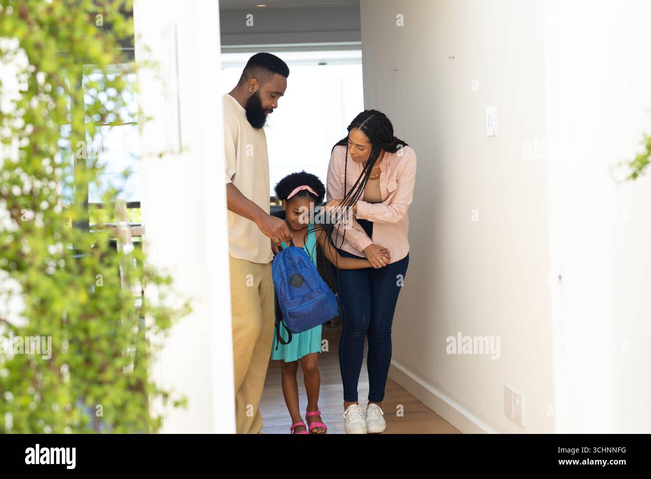 Genitori che aiutano la figlia con lo zaino, si preparano per la scuola in corridoio Foto Stock