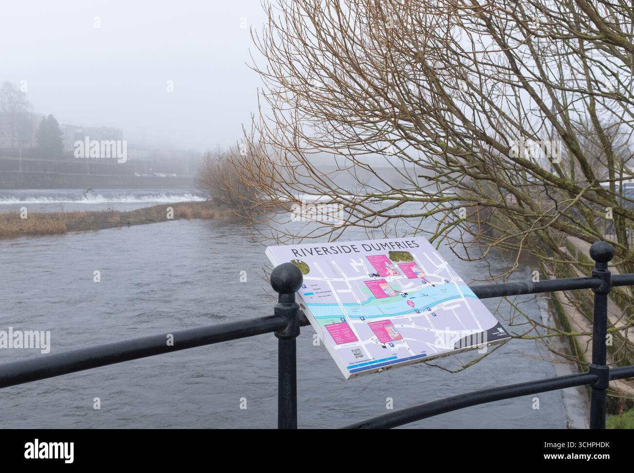 6 febbraio 2025, vista del fiume Nith e del centro cittadino di Dumfries, Scozia, con un'esposizione di informazioni pubbliche e un albero in primo piano. Foto Stock