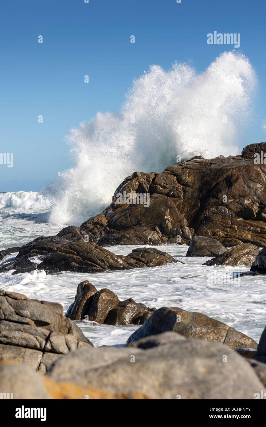Big Ocean Wave che si schianta contro Rock con spettacolare Splash che mostra il potere del mare sotto cieli azzurri e coste rocciose Foto Stock