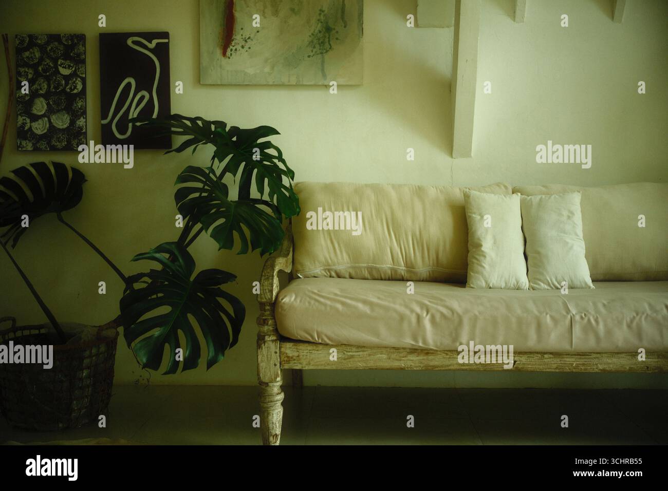 Un divano in legno rustico con cuscini beige, piante interne e decorazioni artistiche Foto Stock