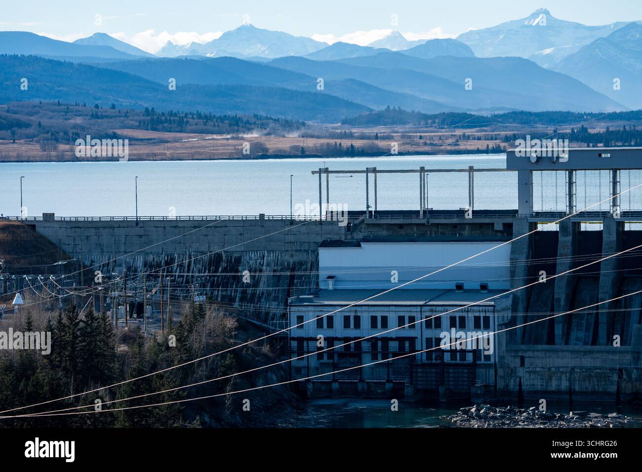 Diga idroelettrica che genera elettricità con linee elettriche che si affacciano sul lago e sulle lontane Montagne Rocciose canadesi vicino a Cochrane, Alberta, Canada. Foto Stock