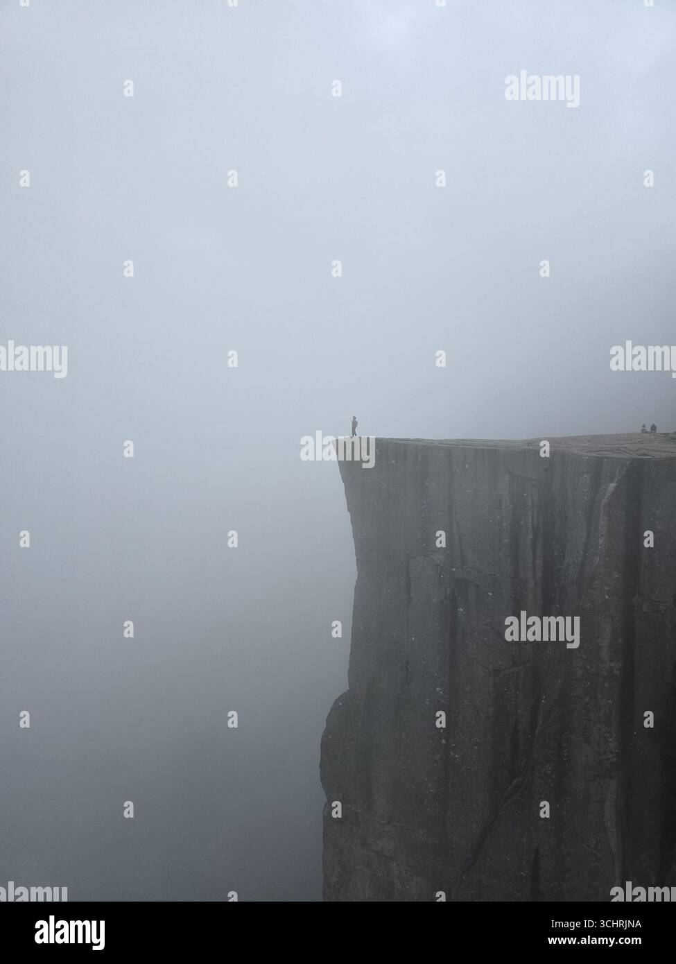 La maestosa scogliera di Preikestolen si innalza drammaticamente sopra i fiordi della Norvegia, offrendo vedute mozzafiato. Gli avventurieri si stagliano sul bordo, avvolti da una misteriosa nebbia, creando un'atmosfera maestosa. Foto Stock