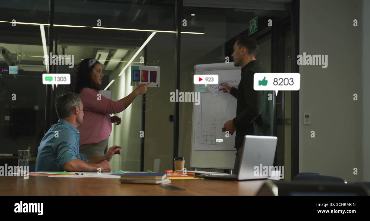 Analizzando le metriche, tre colleghi che puntano alla carta a colori nella sala conferenze in vetro, con un laptop Foto Stock
