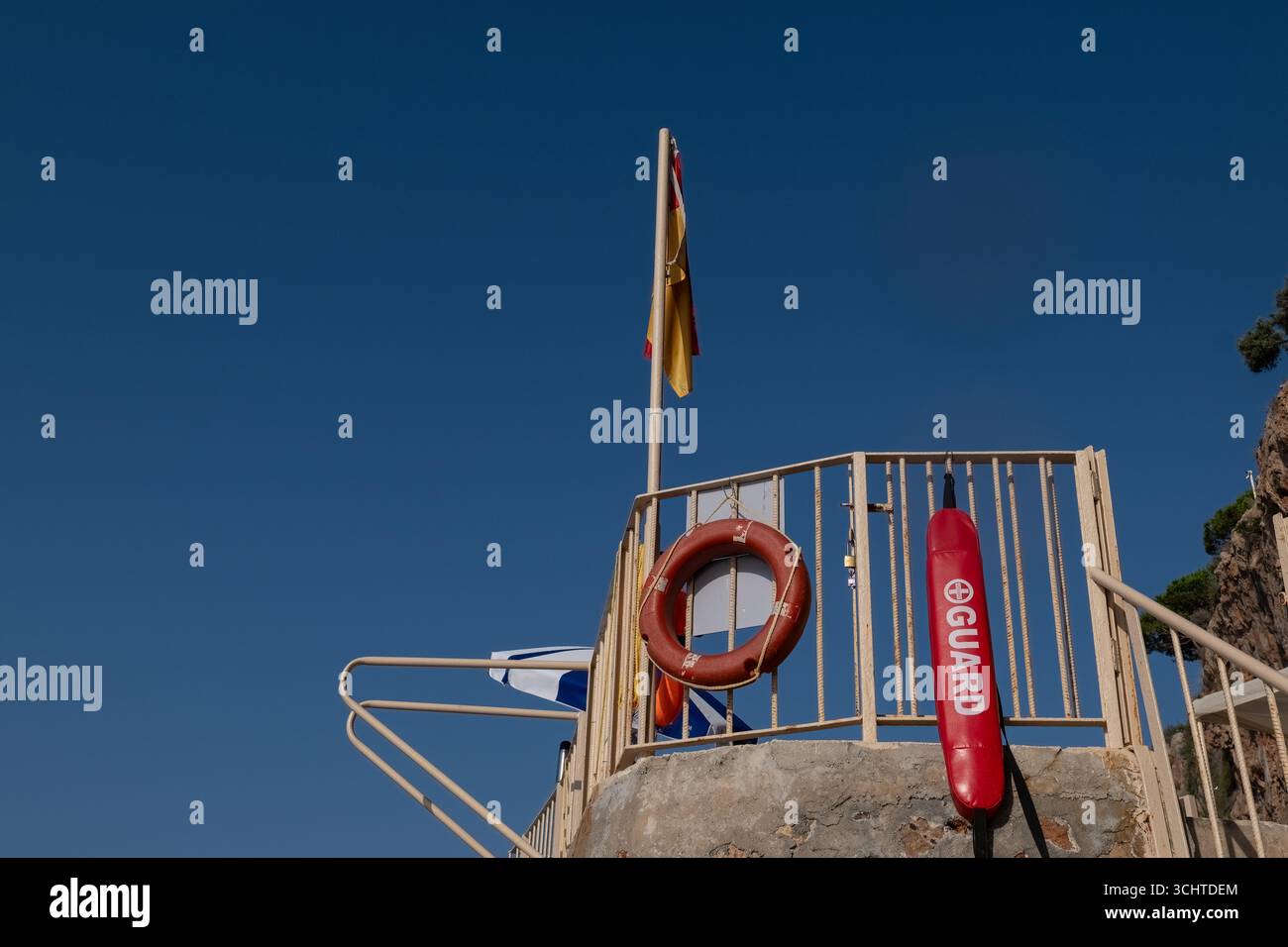 Stazione di salvataggio con equipaggiamento di salvataggio e bandiere in una giornata di sole, simboleggiando la sicurezza costiera e la vigilanza per i naviganti. Foto Stock