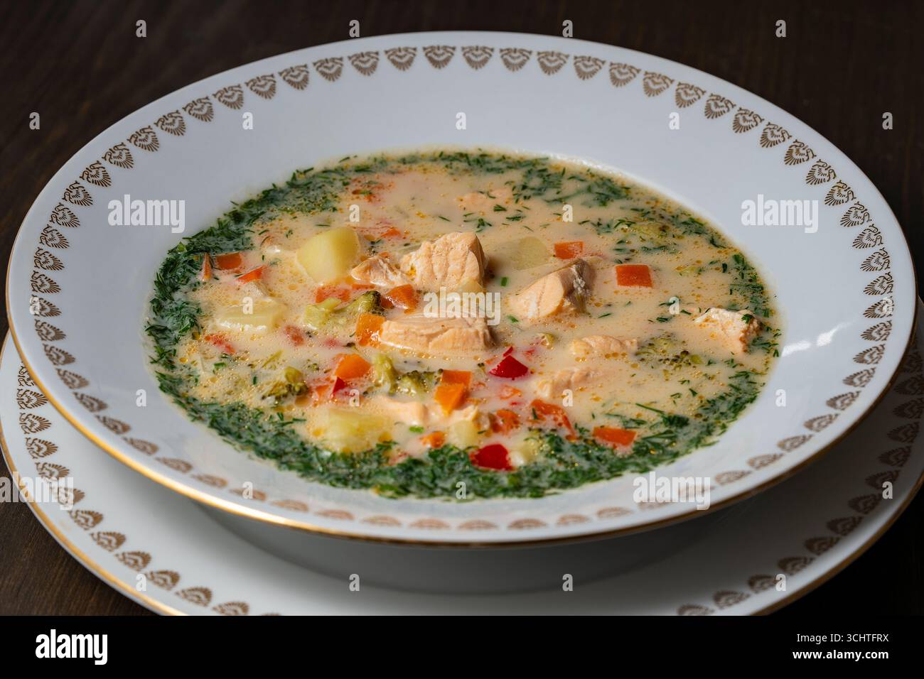Zuppa fresca di pesce di salmone cremosa con patate, carote, broccoli, peperoni e cipolle in un piatto di ceramica su un tavolo di legno, da vicino. Una cena deliziosa Foto Stock