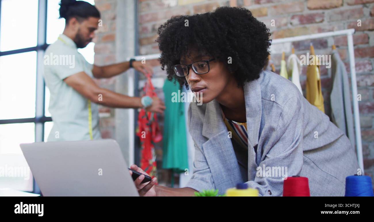 Stilista di moda donna appoggiata sulla scrivania tenendo lo stilo in un monolocale loft, con laptop e metro a nastro Foto Stock