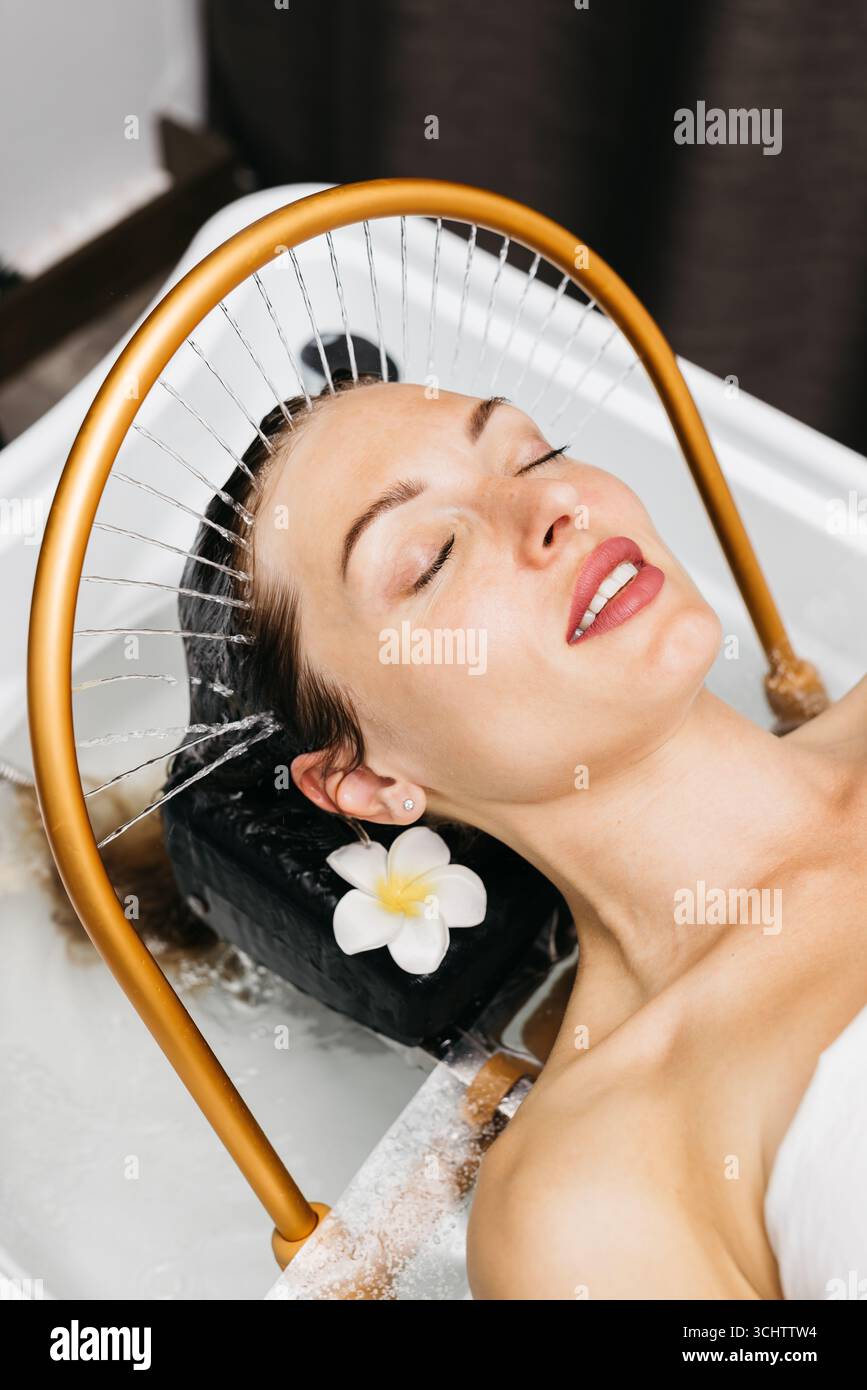 Donna che sperimenta la terapia con idromassaggio in un tranquillo ambiente termale, con acqua rilassante e delicati accenti floreali, promuovendo relax e benessere Foto Stock