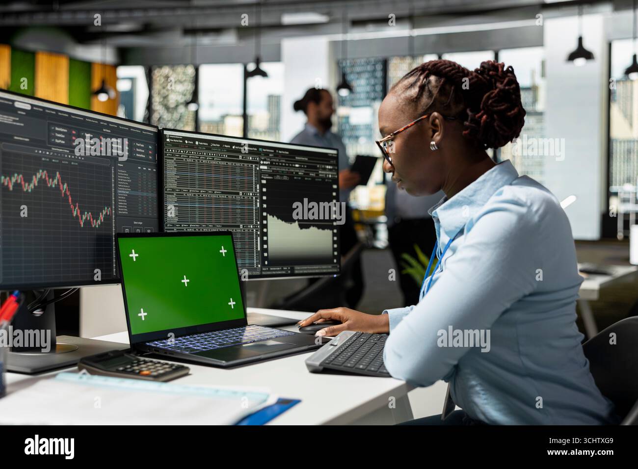 Il dipendente di un'azienda proprietaria utilizza un notebook con schermo verde in ufficio per monitorare i grafici delle scorte in tempo reale. Donna afroamericana che usa un notebook con chiave Chroma con software finanziario nello spazio di lavoro aziendale Foto Stock