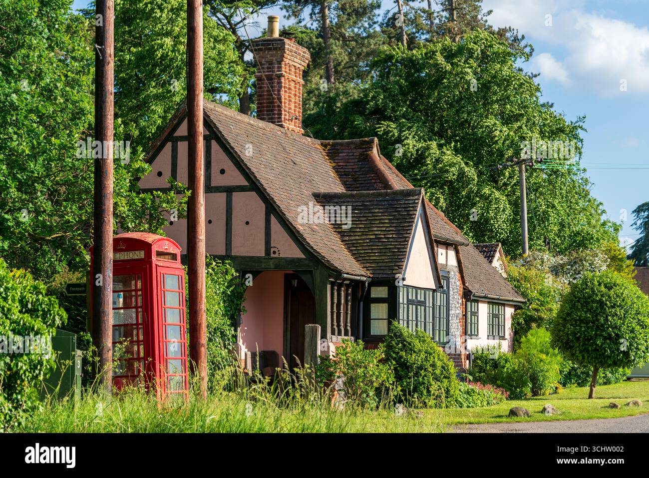 Una tradizionale casa di campagna inglese si erge graziosamente accanto ad una vecchia cabina telefonica rossa nella campagna del Suffolk, mescolando fascino rurale e patrimonio culturale Foto Stock