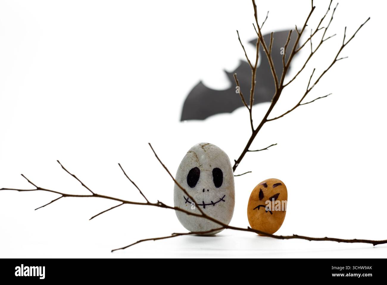 Due pietre dipinte in modo unico che ricordano i personaggi di Halloween si trovano sui rami. La silhouette di un pipistrello si sposta sullo sfondo. Questo allestimento natalizio cattura t Foto Stock