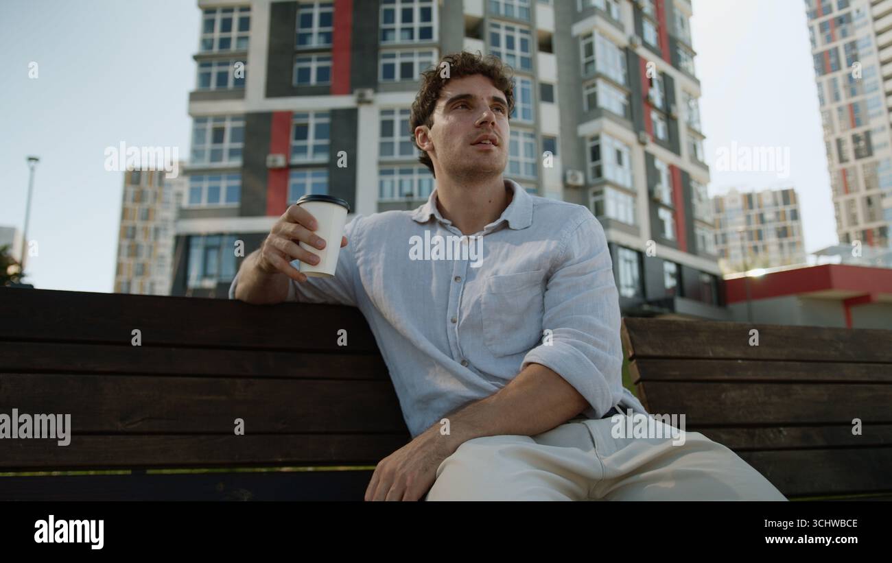 Uomo europeo caucasico seduto sulla panchina maschio che tiene tazza pausa caffè bere takeaway ordine cliente acquirente rilassarsi gustoso drink Guy studente uomo d'affari Foto Stock